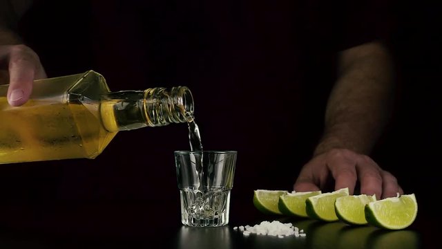 Slow mo. The bartender's hand pours cold tequila from a bottle into a shot
