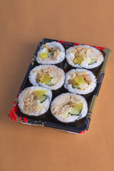 A box of sushi rolls on the yellow table.