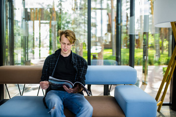 Handsome young man with blond hair sitting and reading a magazine