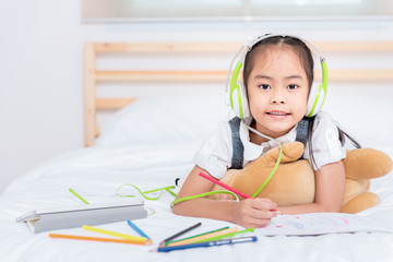 Cute asian little girl doing homework,writing with colourful pencils on bed at home. Elegant design for kid playing, preschool learning and creative art education concept.