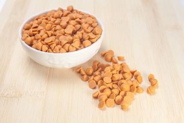 Butterscotch chips in white bowl on wooden background