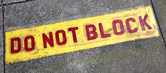 Red on yellow DO NOT BLOCK sign stenciled on driveway.