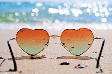 Heart-shaped sunglasses on the wet sand, beach at the seaside. Travel and vacation concept