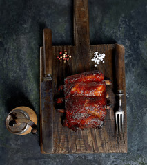 Delicious barbecued ribs seasoned with a spicy basting sauce and served with chopped fresh vegetables on an old rustic wooden chopping board in a country kitchen