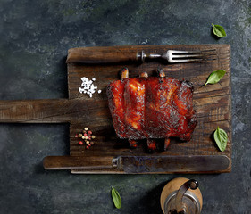 Delicious barbecued ribs seasoned with a spicy basting sauce and served with chopped fresh vegetables on an old rustic wooden chopping board in a country kitchen