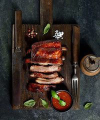 Delicious barbecued ribs seasoned with a spicy basting sauce and served with chopped fresh vegetables on an old rustic wooden chopping board in a country kitchen