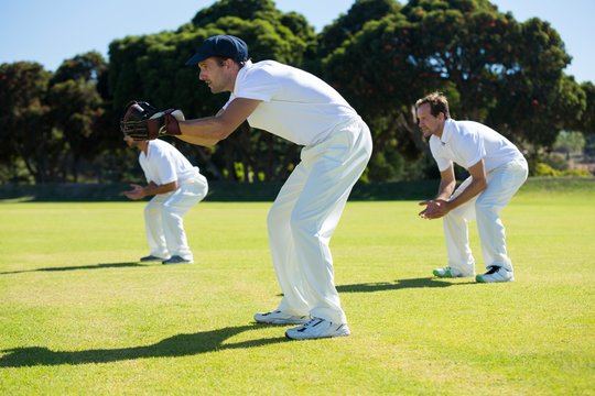 Side view of players bending while playing cricket at field