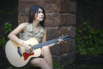 Woman siting and playing guitar, brick wall background