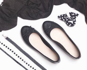 Obraz premium Black faux leather ballet flats with black accessories like scarf, bracelet and necklaces on white background. Flat lay. Top view.