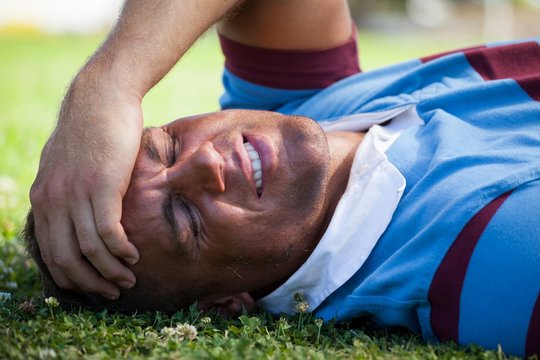 Injured rugby player with eyes closed lying on field - Powered by Adobe