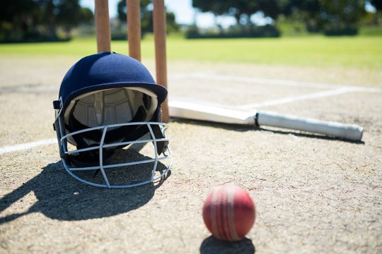 Sports helmet and ball with bat by stumps on pitch