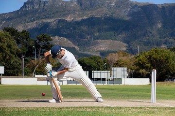 Full length of batsman playing cricket on field against mountain - obrazy, fototapety, plakaty