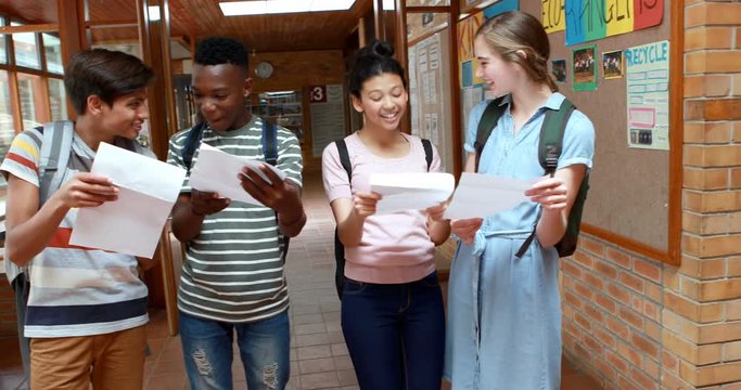 Happy classmates looking at grade cards in corridor