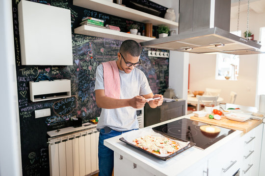 Man taking a photo with his phone to the handmade pizza at home