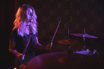 Confident female drummer performing on illuminated stage 