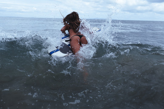 A sexy young woman jumps into the surf on her surfboard