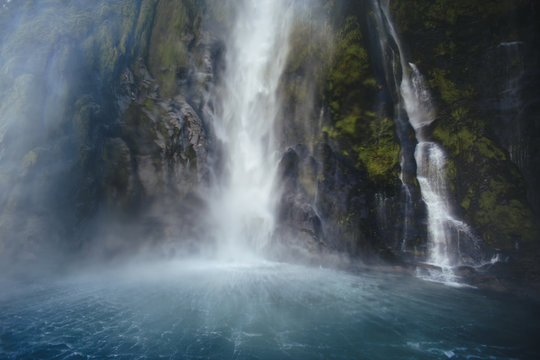 A large waterfall pours into the basin of Milford Sound, New Zealand 