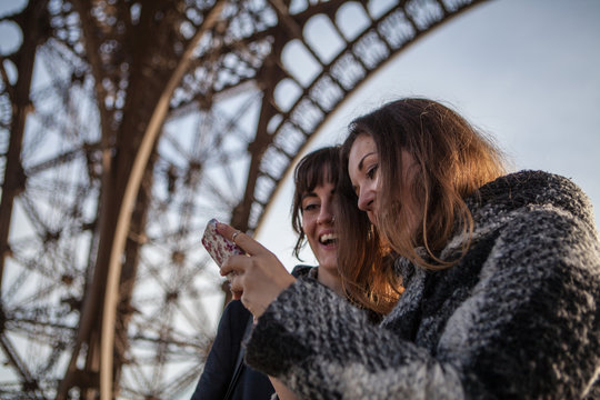 Two young women looking at a mobile phone under the Eiffel Tower in Paris