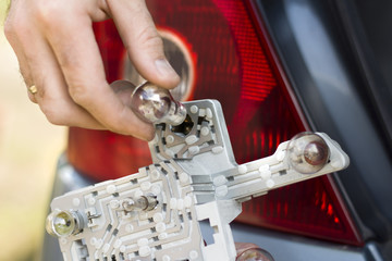 Dłoń mechanika wkłada żarówkę do wkładu lampy tylnej w samochodzie. - obrazy, fototapety, plakaty