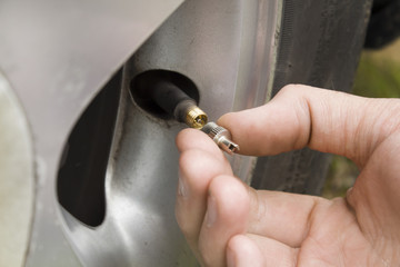 Dłoń mechanika odkręca zakrętkę wentyla w kole samochodu. - obrazy, fototapety, plakaty