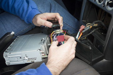 Ręce elektryka samochodowego podłączają kostkę przewodów od radia do instalacji elektrycznej samochodu. Elektryk samochodowy podłącza radio w samochodzie  - obrazy, fototapety, plakaty