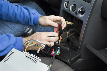 Ręce elektryka samochodowego podłączają kostkę przewodów od radia do instalacji elektrycznej samochodu. Elektryk samochodowy podłącza radio w samochodzie 