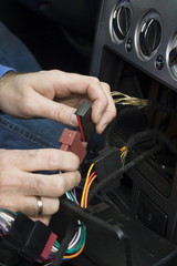 Ręce elektryka samochodowego podłączają kostkę przewodów od radia do instalacji elektrycznej samochodu. Elektryk samochodowy podłącza radio w samochodzie  © Tomasz
