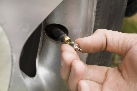 Dłoń mechanika odkręca zakrętkę wentyla w kole samochodu.