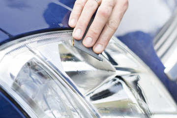 Dłoń mechanika samochodowego poleruje papierem ściernym i wodą zmatowiałe szkło reflektora....