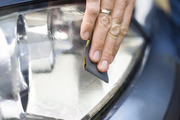 Dłoń mechanika samochodowego poleruje papierem ściernym i wodą zmatowiałe szkło reflektora. Auto detailing. Odnawianie szkła reflektora. Polerowanie papierem ściernym i wodą. - obrazy, fototapety, plakaty