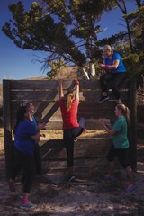 Woman being cheered to climb a wooden wall 