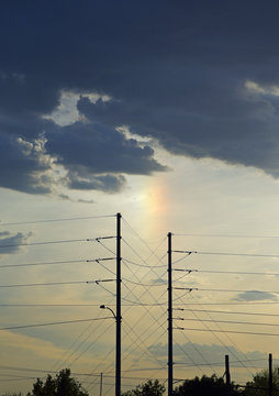 Nebensonne und dunkle Wolken hinter Stromleitungen am Abendhimmel