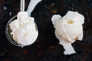 Top view of ice cream scooper with balls of ice cream on black rustic background.
