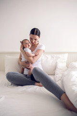 mother with her newborn son in hands sitting on a big white bed