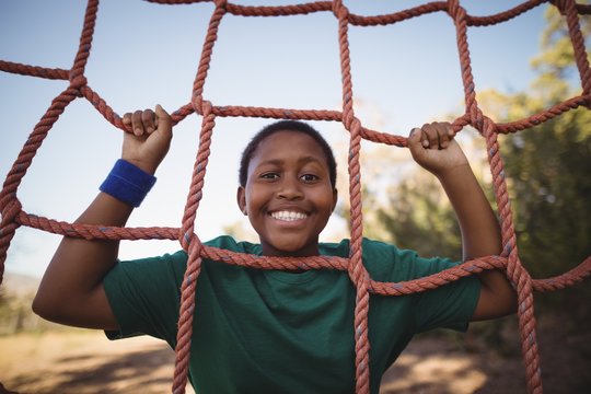 Portrait of happy boy leaning on net during obstacle course