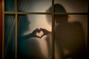 Two silhouettes representing love with a heart behind a window