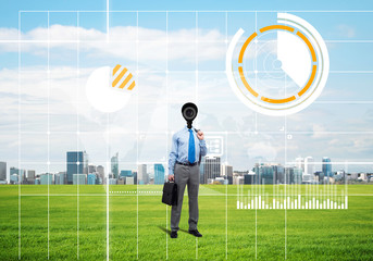 Camera headed man standing on green grass against modern cityscape