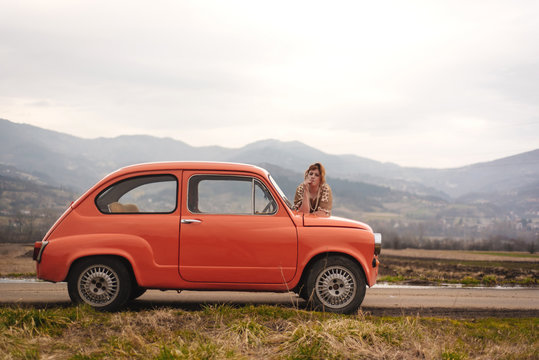 Young woman standing next to the vintage car in the countryside