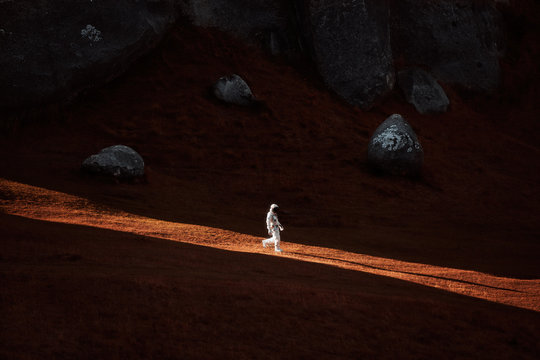 A lone astronaut descends the side of a mountain