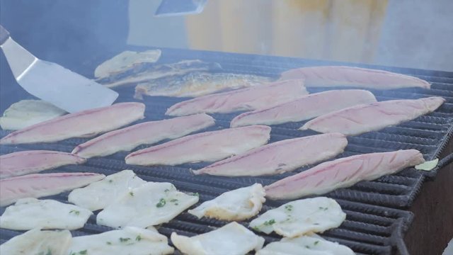 The chef toils over an open grill frying fish, rapans and squid. Cooking mackerel fillet at grill for fish durum.