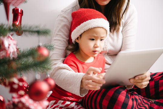Toddler girl and her mother using digital PC by christmas tree