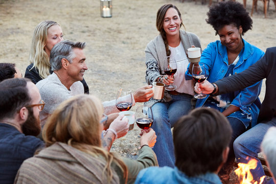 Group of friends toasting red wine while sitting around fire pit