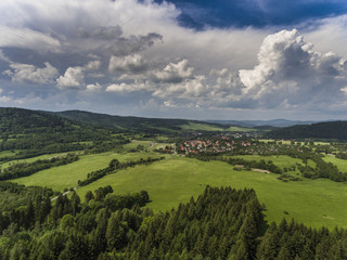 Obraz premium Aerial view of the summer time in mountains near Stronie Slaskie town in Poland. Pine tree forest and clouds over blue sky. View from above.