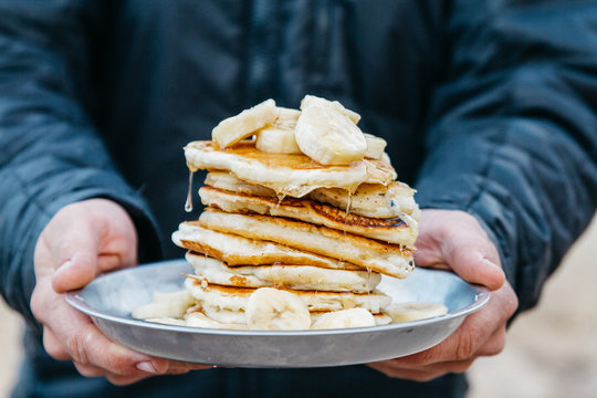 young man holds pile of pancakes on a plate while camping