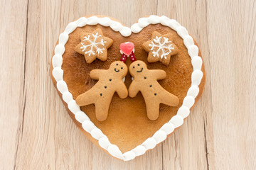 Close up of a cute Gingerbread heart decorated with Gingerbread Men, Gingerbread Stars and a Christmas Tree Cookie on light brown wooden background.