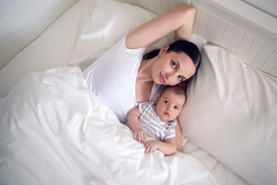 mom with a newborn son lying on a white bed