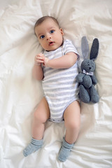 the child lies on his back on a big white bed with soft toy rabbit