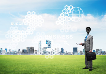 Camera headed man standing on green grass against modern cityscape