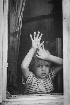 Boy looks out of an old wooden window
