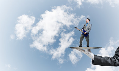 Naklejka na ściany i meble Businessman on metal tray playing electric guitar against blue sky background